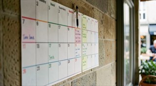 Jaarplanner aan een cafémuur met gekleurde markeringen per maand en een pen aan een touwtje.
