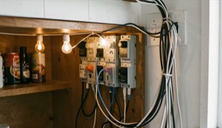 Rij ontvangers en kabels achter een barkast, lampjes branden, netjes gebundelde snoeren aan de muur.