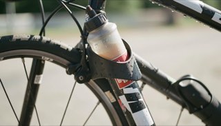 Close-up van een bidon in de houder van een racefiets, waterdruppels op het frame in zonlicht.